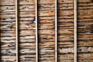 Attic rafters and plywood roof decking show dark water stains and softened wood beneath a leaking roof.